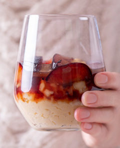 Woman's hand holding out a wine glass with rice pudding and plums in it