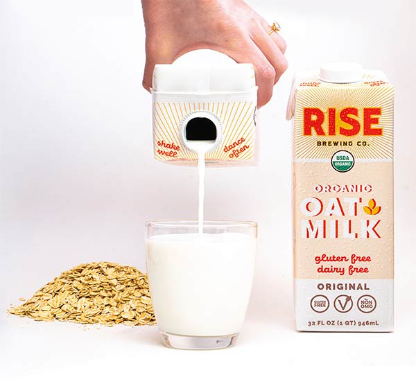 Rise Oat Milk being poured into a glass with a pile of oats on the side