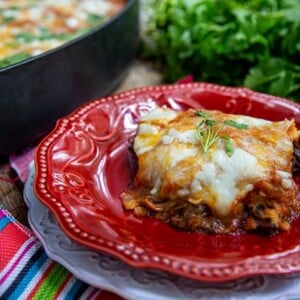 Short Rib Enchiladas on top of a decorative red plate with a colorful striped napkin next to it