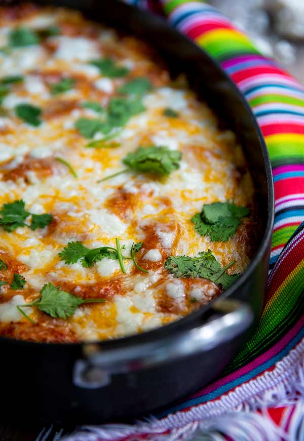 Short Rib Enchiladas in a black casserole dish on top of a colorful Mexican-style tablecloth