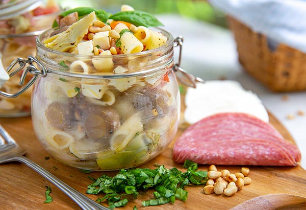 Summer Antipasto Pasta Salad in a glass jar on top of a wooden cutting board