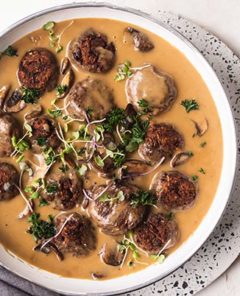 Vegan Swedish Meatballs in gravy in a white dish with a white and black speckled plate underneath