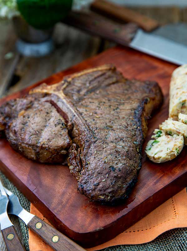 T-Bone Steaks with Savory Compound Butter on a wooden cutting board.