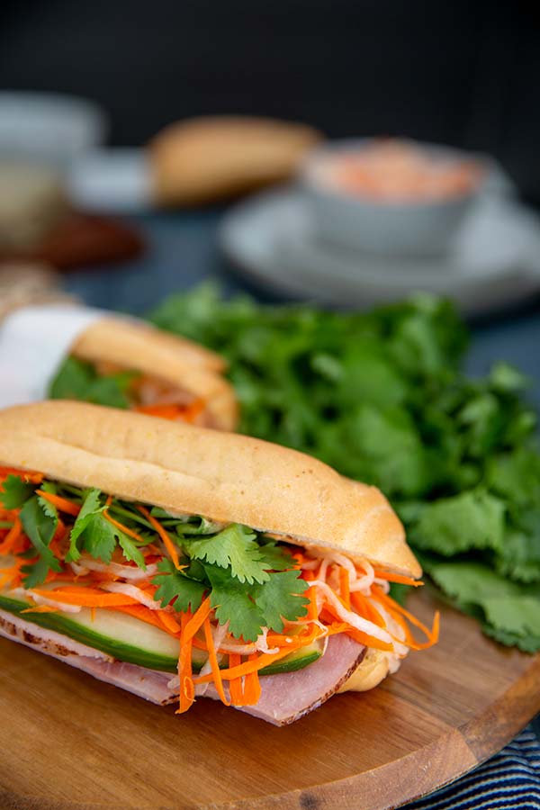 Banh Mi Sandwich on a wooden cutting board with a bunch of cilantro in the background
