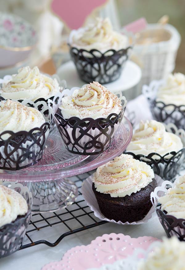 Mocha Cupcakes with white frosting in decorative black cupcake liners on a light pink serving pedestal