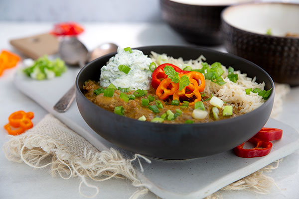 Pork Curry with green onions on top in a black bowl set on a white serving board