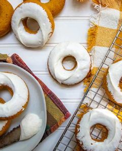 Overhead view of frosted Pumpkin Spice Donuts on a plate and metal cooling rack on top of yellow plaid tablecloth