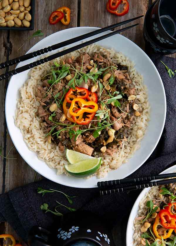 Thai Green Curry on a bed of rice topped with peppers, microgreens and lime wedges on a white plate with black chopsticks