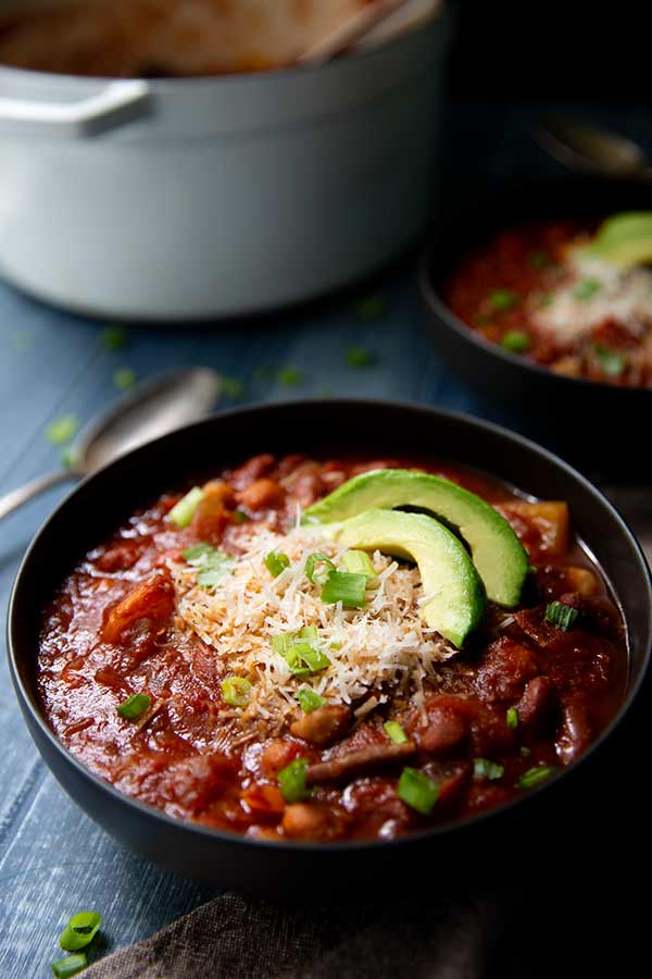 Vegetarian Chili in a black bowl topped with sliced avocados and green onion