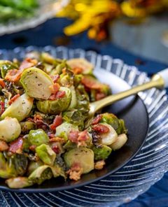 Bacon and Maple Roasted Brussels Sprouts on a black plate set over a clear serving plate on a navy blue tablecloth