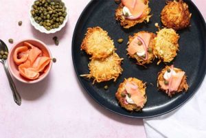 Classic Latkes on a black plate topped with cream cheese and lox