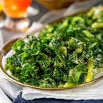 Closeup of Creamed Kale on a clear oval serving tray with white cloth napkins underneath on a dark blue background