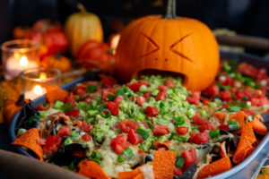 Carved pumpkin face with guacamole coming out of its mouth onto Halloween Nachos