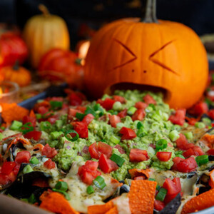 Carved pumpkin face with guacamole coming out of its mouth onto Halloween Nachos