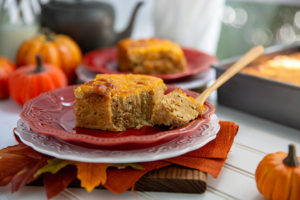 Leftover Stuffing Breakfast Bake on a red plate with a white plate underneath and fall leaves and pumpkins in the background