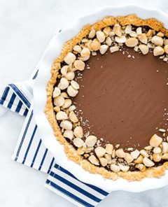 Macadamia Nut Chocolate Pie with Coconut Crust in a white ceramic pie pan on a white marble background with a navy and white striped napkin underneath