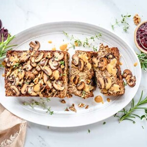 Gluten-free Nut Roast on a white plate on a white marble background with fresh herbs and leaves around the platter