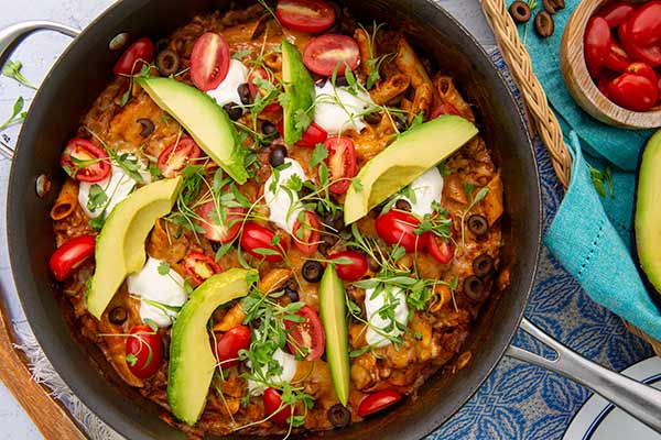 Closeup of One Pot Enchilada Pasta with sliced avocados in a black and stainless steel skillet