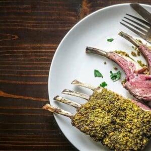 Overhead view of Pistachio Crusted Rack of Lamb on a white plate on a brown wooden background