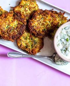 Overhead of Potato-Zucchini Latkes with Parsley Lime Sauce on a rectangular white plate on a pink background