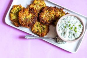 Overhead of Potato-Zucchini Latkes with Parsley Lime Sauce on a rectangular white plate on a pink background