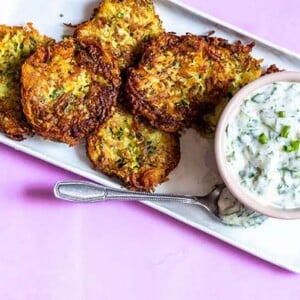 Overhead of Potato-Zucchini Latkes with Parsley Lime Sauce on a rectangular white plate on a pink background