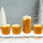 Pumpkin Apple Soup Shooters with Coconut Cream lined up in different sized shot glasses on a silver and white holiday background