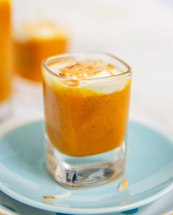 Closeup of Pumpkin Apple Soup Shooter with Coconut Cream in a shot glass on a light blue plate