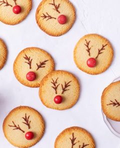 Rudolph Cookies scattered across a white background with a red mug of hot cocoa