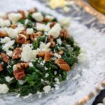Closeup of Sauteed Spinach with Feta and Walnuts on a clear glass plate lines with gold