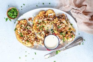 Spiced Cauliflower Steaks on a white plate sprinkled with fresh herbs