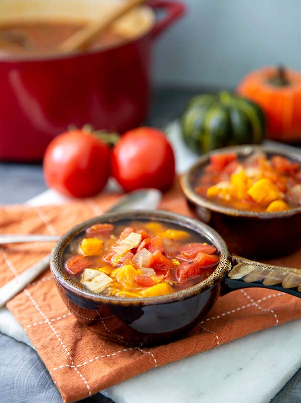 Sweet Potato & Leftover Turkey Soup in bowls on an orange placemat with tomatoes and pumpkins in the background