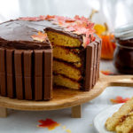 Layered yellow cake with chocolate frosting with a slice cut out and edible fall leaves on top