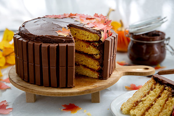 Layered yellow cake with chocolate frosting with a slice cut out and edible fall leaves on top