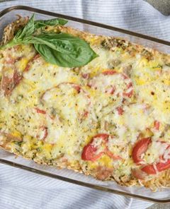 Breakfast Casserole in a rectangular glass baking with on a white and gray striped cloth napkin with fresh basil leave around it