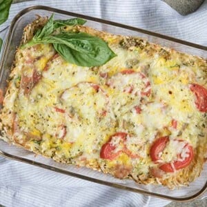 Breakfast Casserole in a rectangular glass baking with on a white and gray striped cloth napkin with fresh basil leave around it