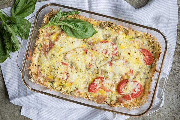 Breakfast Casserole in a rectangular glass baking with on a white and gray striped cloth napkin with fresh basil leave around it