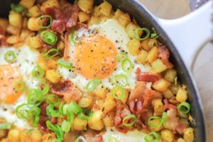 Closeup of Breakfast Hash with over easy eggs and sliced green onions in a white skillet