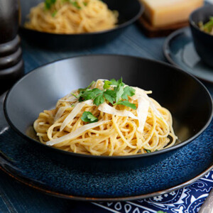 Creamy Garlic Parmesan One Pot Pasta topped with parsley in a black bowl with dark blue plate underneath