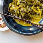 Curried Collards in a dark blue bowl with brown chopsticks on a white background