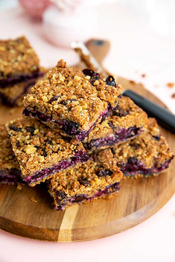 Closeup of Granola-Topped Blueberry Pie Bars stacked on a round wooden cutting board