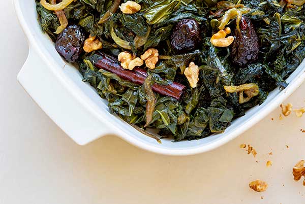Closeup of Moroccan Style Winter Greens with walnuts and cinnamon sticks in a white casserole dish