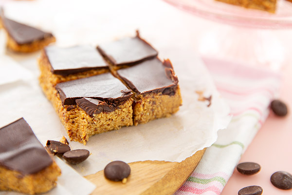 Peanut Butter Protein Bars on parchment paper on a light wooden cutting board set on a baby pink background