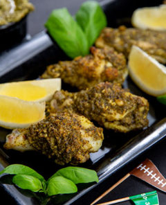 Pesto Chicken Wings on a black rectangular serving tray with lemon wedges and basil leaves and football themed flag toothpicks