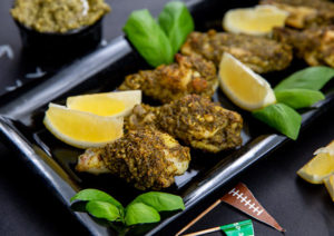 Pesto Chicken Wings on a black rectangular serving tray with lemon wedges and basil leaves and football themed flag toothpicks