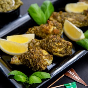 Pesto Chicken Wings on a black rectangular serving tray with lemon wedges and basil leaves and football themed flag toothpicks