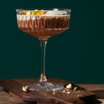 Pistachio Chocolate Mousse in a fancy cocktail glass set on a dark wood cutting board with a dramatic dark green background