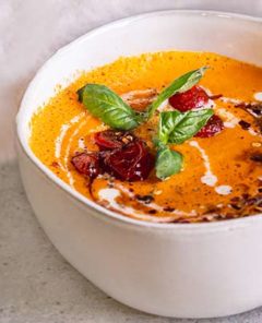 Roasted Tomato Carrot Soup in a white bowl drizzled with dairy free milk and garnished with basil leaves