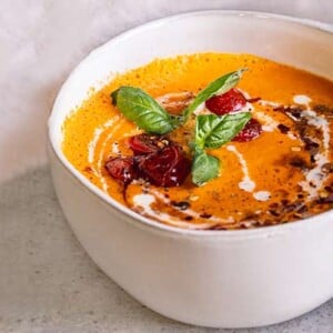Roasted Tomato Carrot Soup in a white bowl drizzled with dairy free milk and garnished with basil leaves