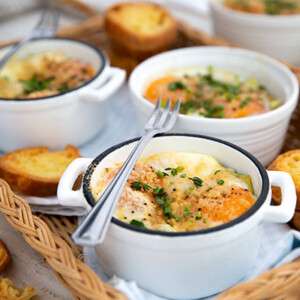 Spinach Artichoke Baked Eggs in white ramekins in a wicker basket tray